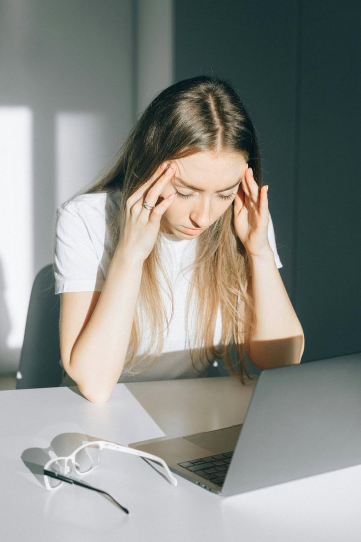Headache woman holds head and sits in front of laptop in office environment.
